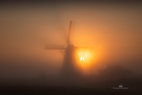 De zon komt op achter de molen op een mistige ochtend
