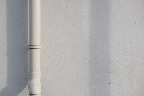 Witte muur met regenpijp en schaduwen