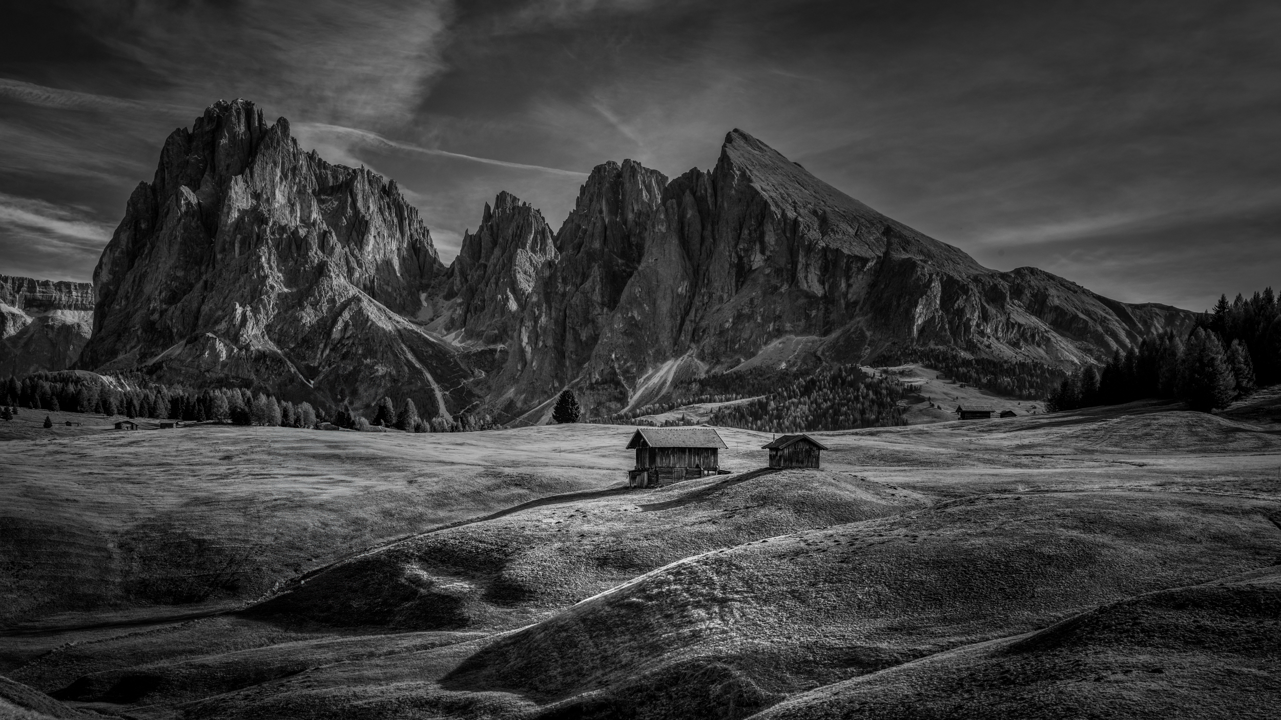 Alpe di Suisi in 'moody' zwart en wit. - Alpe di Suisi in 'moody' zwart wit. 
Twee kleine huisje op de 'seiser alm' in het najaar. 
De zon staat laag aan de hemel wat zorgt voor lange schadu - foto door Teun.R op 10-12-2024 - locatie: Alpe di Siusi, Italië - deze foto bevat: fujifilm, gfx100s ii, gf45-100mmf4 r lm ois wr, iso 80, diafragma ƒ/10, sluitertijd 1/50s, brandpuntafstand 45mm, bergachtige landvormen, berg, heuvel, bergketen, steen, monochrome fotografie, hoogland, wildernis, landschap, woestijn