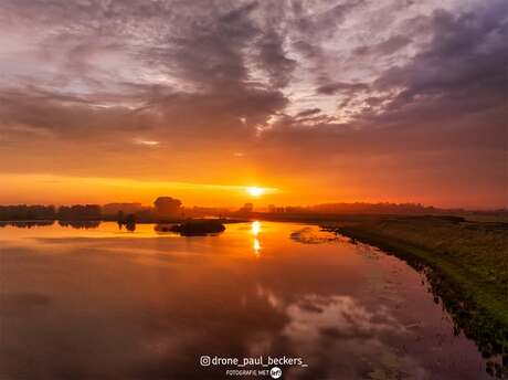 Intens oranje en rood kleuren de lucht boven een stil wateroppervlak in de Ooijpolder 🌅✨