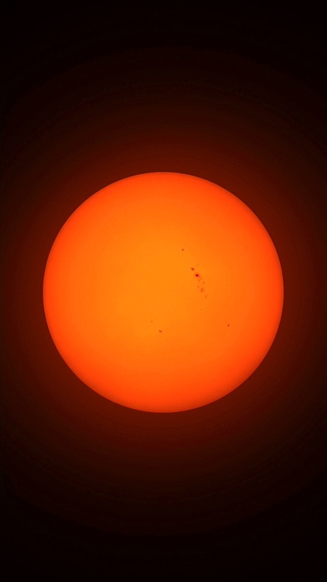 De zon zojuist  achter wat sluierwolken, een paar zonnevlekken zichtbaar.