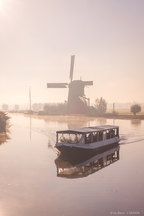 De blokmolen en rondvaartboot van de Kinderdijk met zonsopkomst in de mist