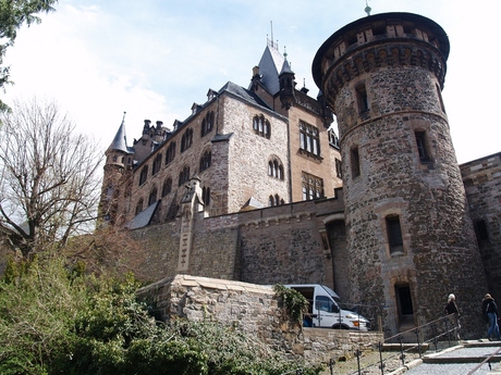Buitenmuur met ronde toren en erboven het kasteel.
