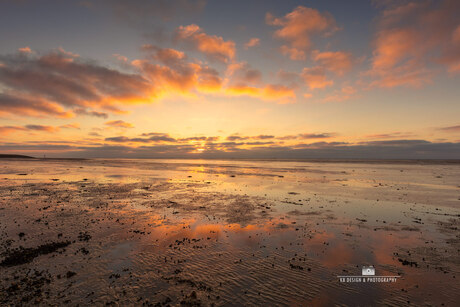 Zonsondergang met wolken en reflectie aan het Wad