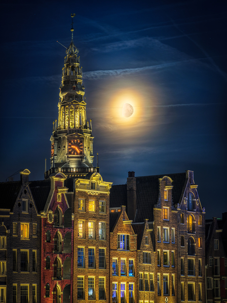 De maan boven de oude kerk op het Damrak in Amsterdam en pakhuizen