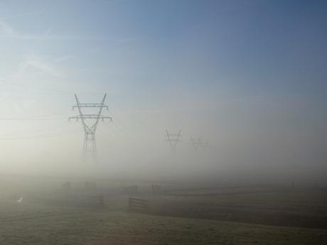 Hoogspanningsmasten doemen op uit ochtendnevel