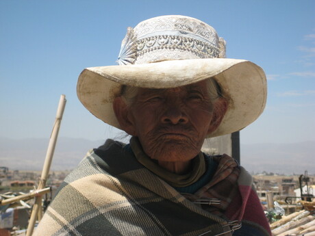 Oude dame met zonnehoed op begraafplaats in Peru
