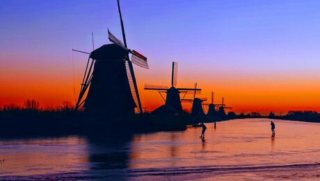 Schaatsers in de opkomende zon tussen de molens van Kinderdijk 