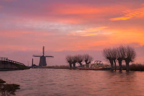 Kaagmolen vergezeld door wilgen en boot onder felgekleurde hemel